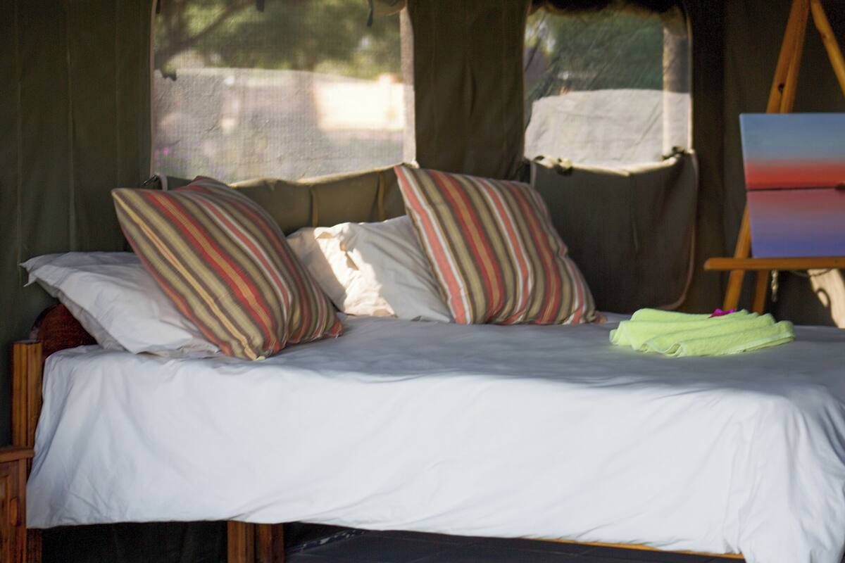 A bed with striped pillows, a painting on an easel, and a neatly folded towel.
