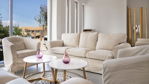 A modern living room with a beige sofa, two white round tables, and a large window offering a view of the outside. - ArionGreen Riviera (Zakynthos)