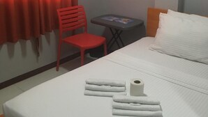 Een hotelkamer met een bed, een klein tafeltje, een rode stoel en een raam met rode gordijnen.