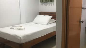 A single bed with white bedding, a wooden headboard, and a green curtain on the window.