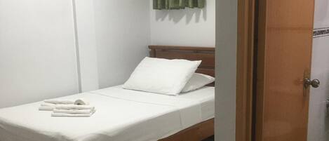 A single bed with white bedding, a wooden headboard, and a green curtain on the window.