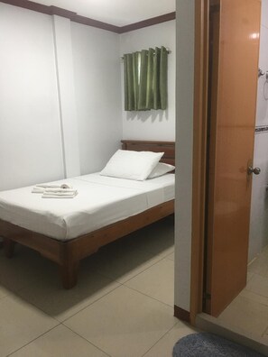 A single bed with white bedding, a wooden headboard, and a green curtain on the window. - Princess Perrine Suites (Davao)
