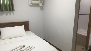 Een net opgemaakt bed met witte lakens en handdoeken, een houten hoofdbord en een wandgemonteerde airconditioning.