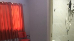 Een kleine, functionele kamer met een bed, een stoel, een douche en een toilet.