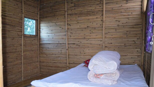 Una habitación pequeña con una cama individual, pared de listones de madera y un ventanal.
