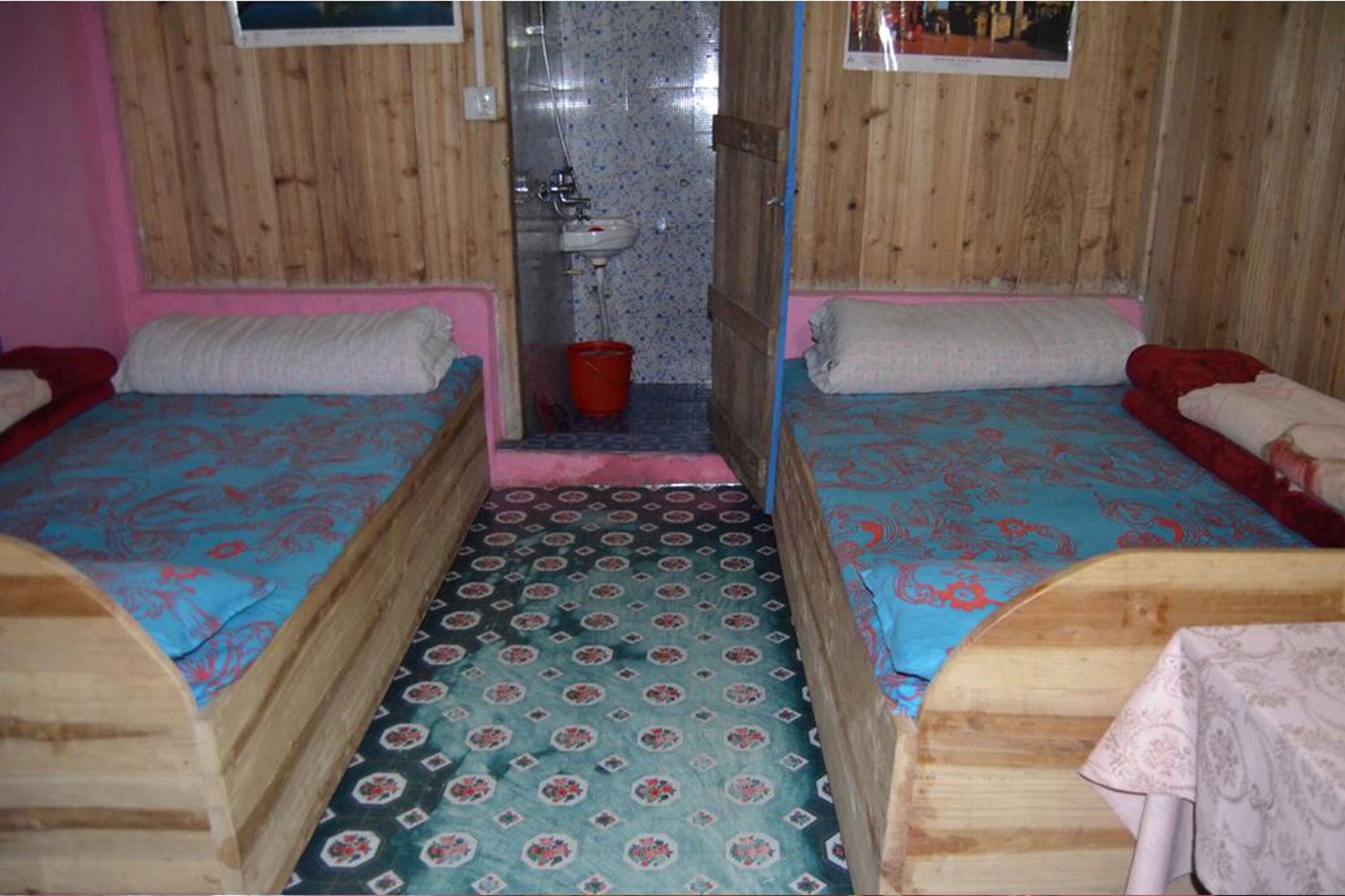 A room with two wooden beds, a small bathroom, and a patterned floor.