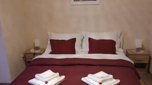 Habitación de hotel con una cama grande, dos almohadas, una colcha roja y dos toallas dobladas sobre la cama.