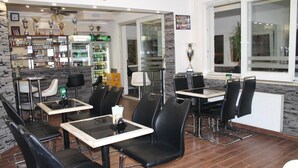 Un restaurante con sillas de cuero negro, mesas blancas, zona de bar y vistas a través de un amplio ventanal.