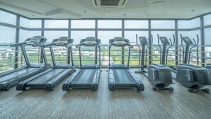 Ett gym med löpband och crosstrainers, stora fönster och utsikt över en stadspanorama.