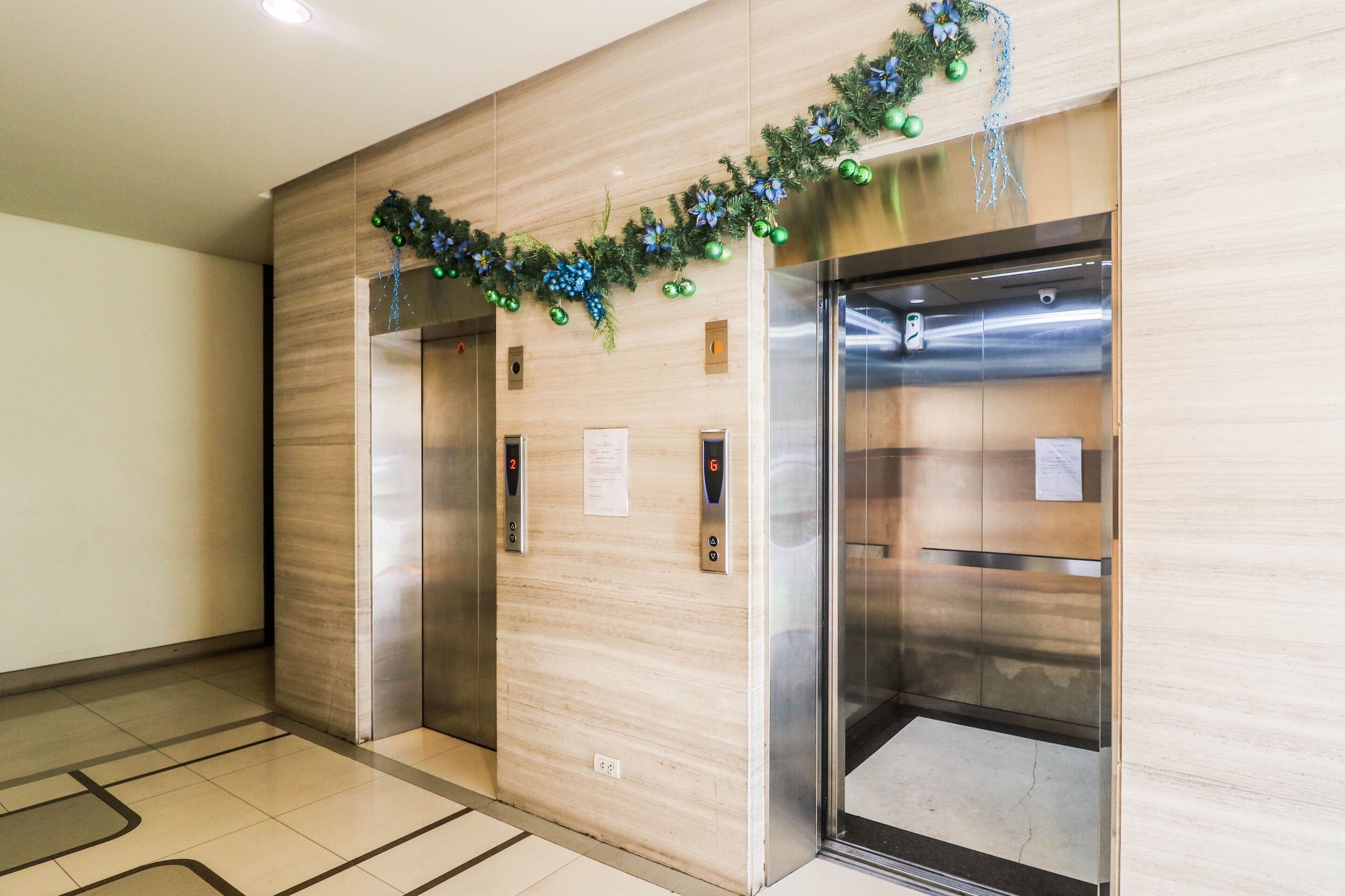 A modern elevator with a wooden panel wall and a metal door, featuring floor indicators and a small sign.