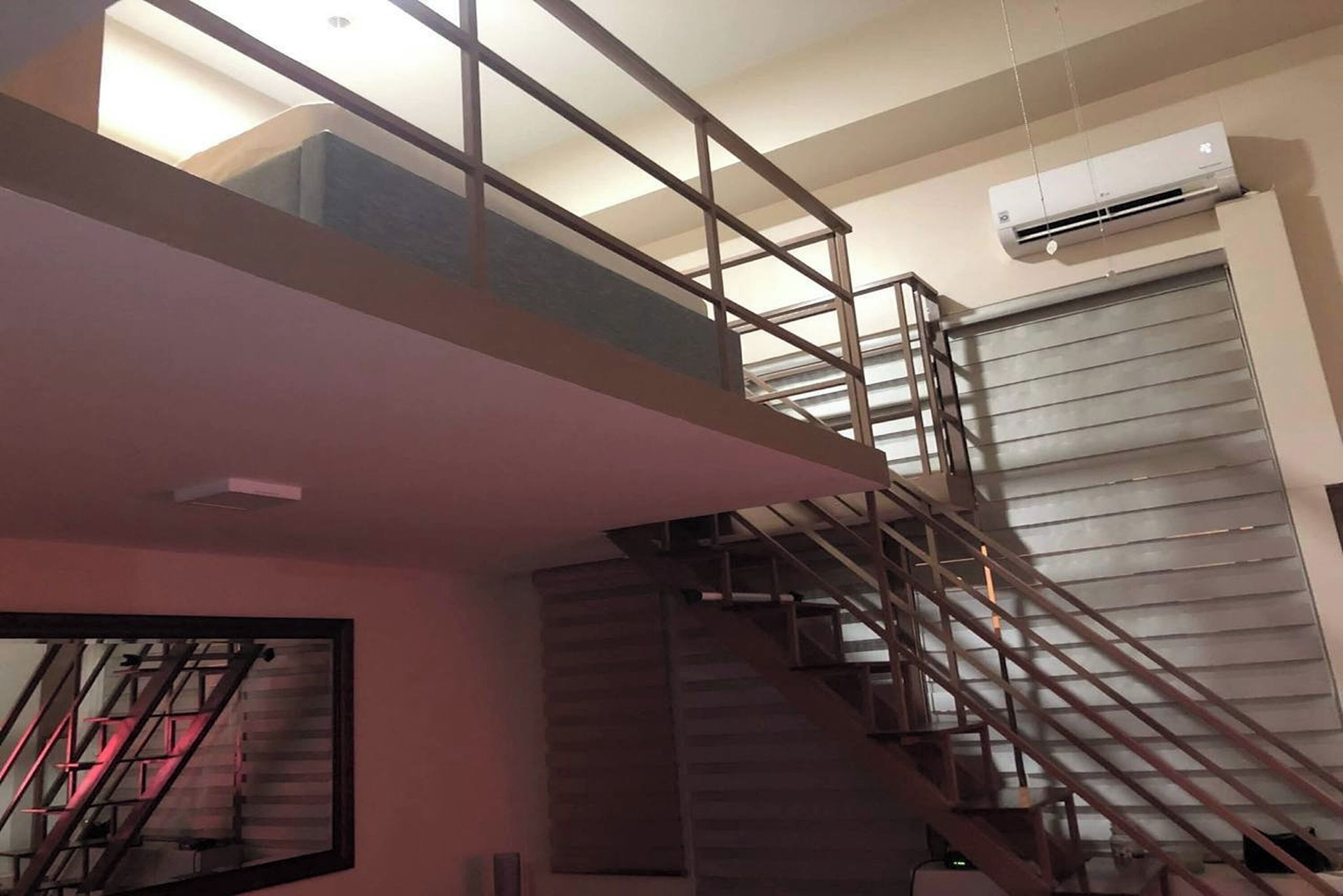 A staircase with metal railings leading to an upper floor, a large mirror on the wall, and an air conditioning unit mounted on the wall.