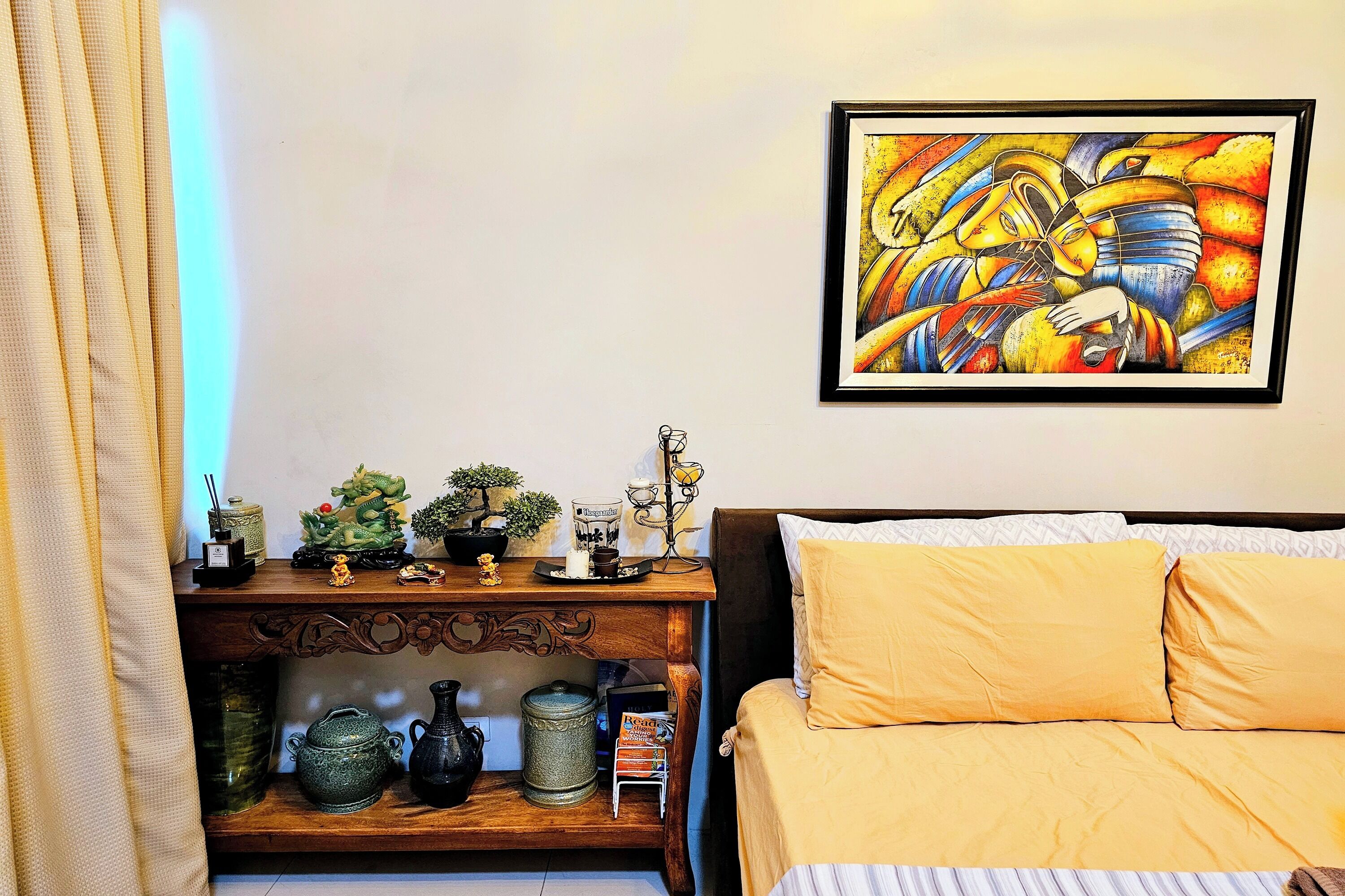 A room with a bed, a wooden console table with decorative items, and a framed painting on the wall.