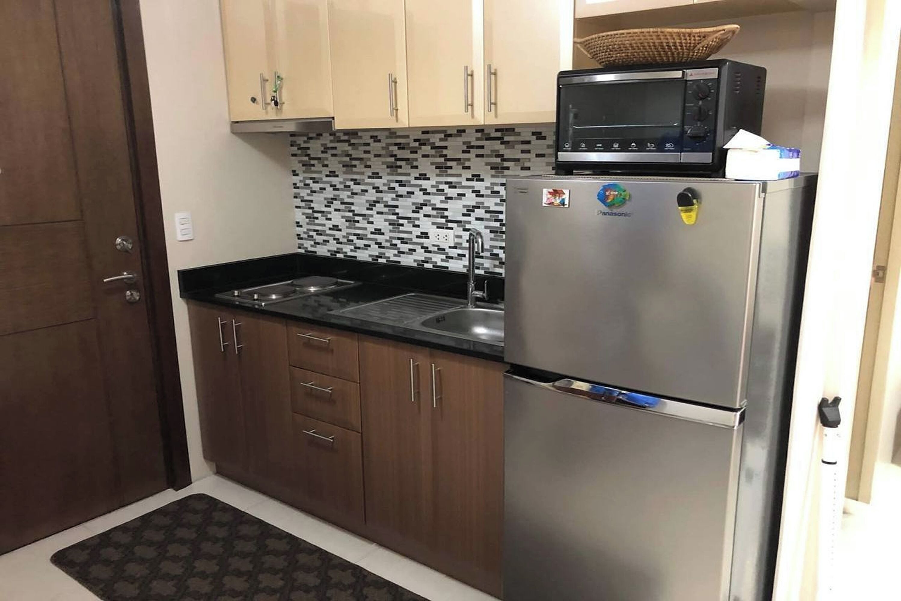 A kitchen with wooden cabinets, a stainless steel refrigerator, a microwave, and a tiled backsplash.