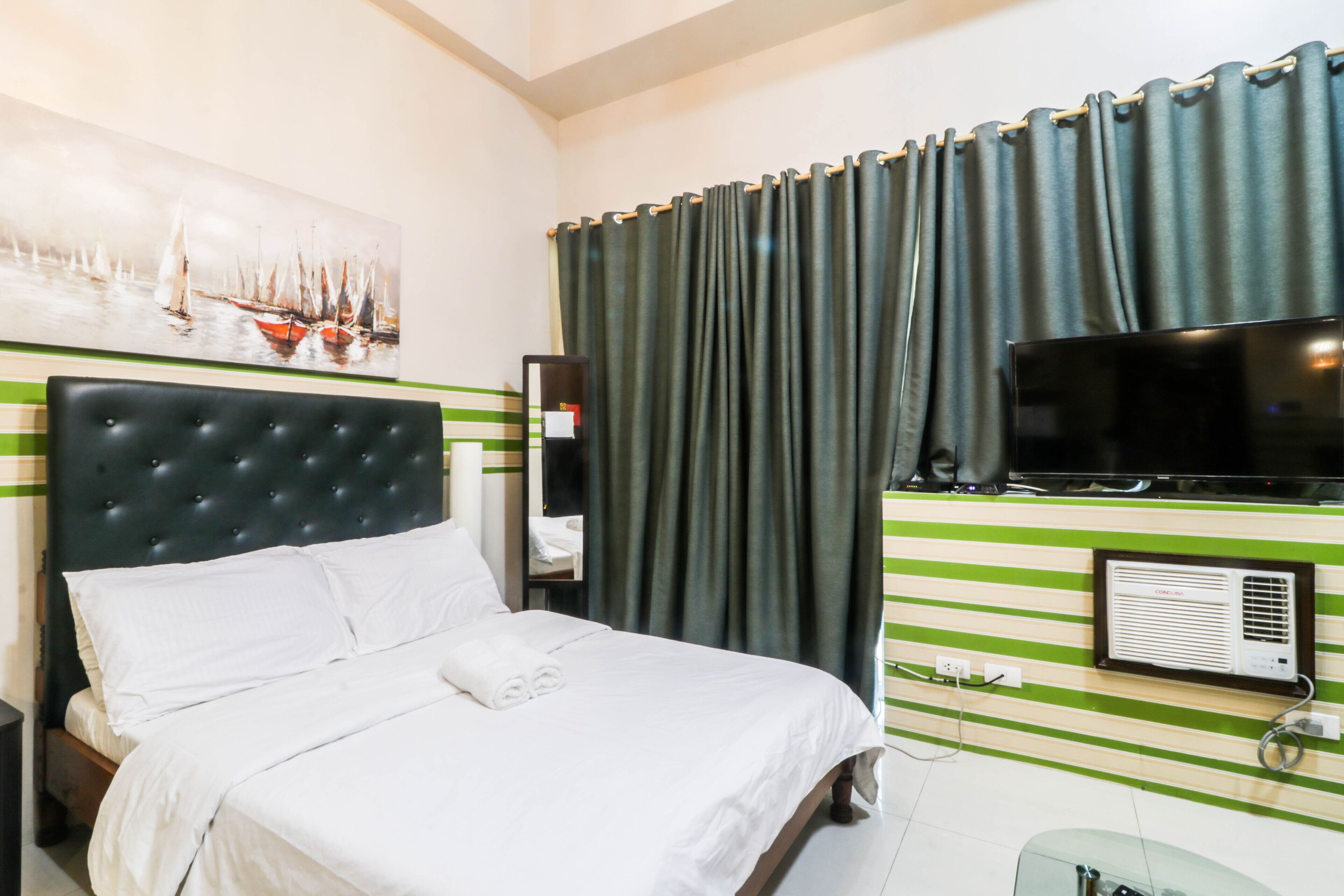 A hotel room with a bed, a television, a painting, and a window with curtains.