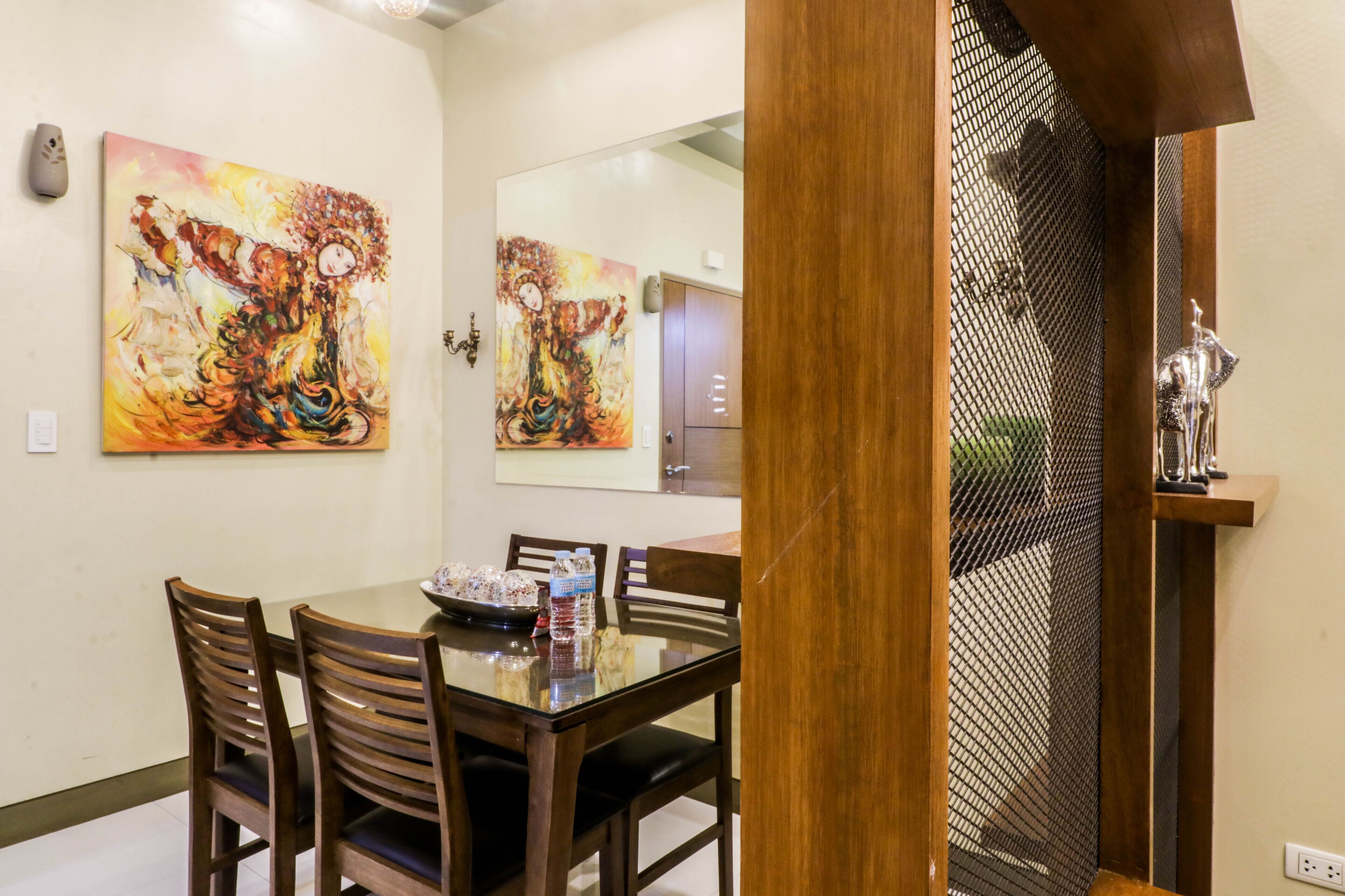 Zona pranzo con tavolo in vetro, sedie in legno e due quadri appesi al muro.