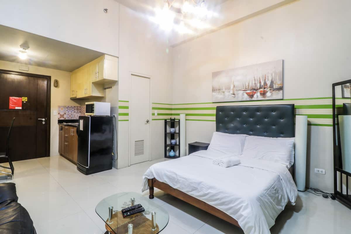 Ein Hotelzimmer mit einem Bett, einem Glastisch, einer Mikrowelle, einem Kühlschrank, einer kleinen Küchenzeile und einem Bild an der Wand.