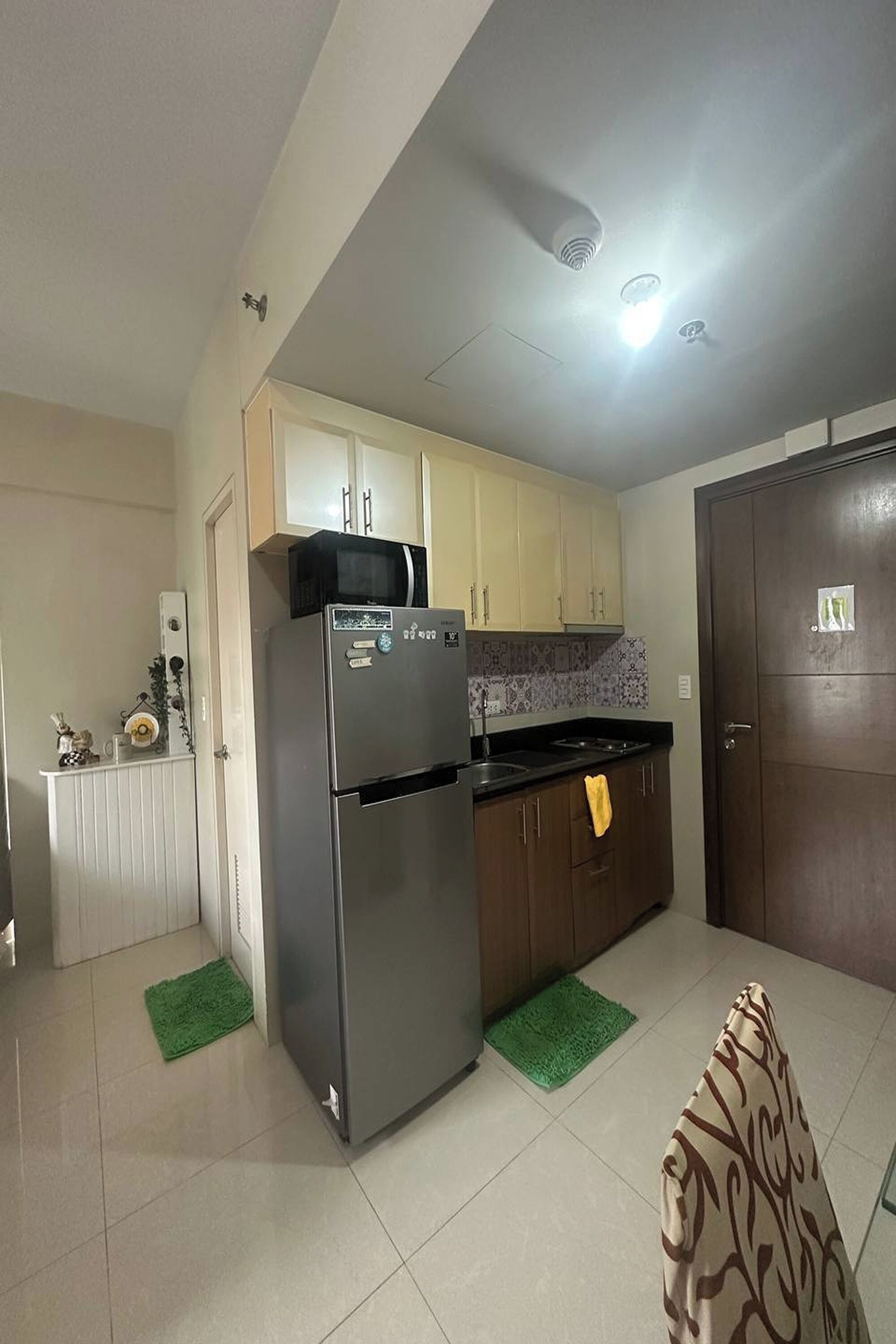 Cocina compacta con refrigerador, microondas y pileta. Hay tapetes verdes en el piso, muebles de madera y una puerta con cerradura.