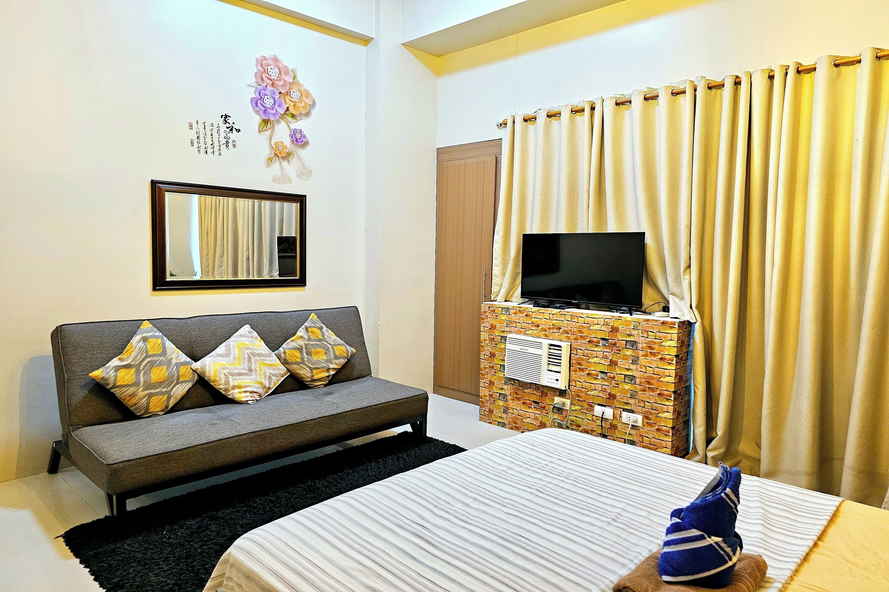 A hotel room with a sofa, a bed, a TV, and a brick-patterned wall unit.