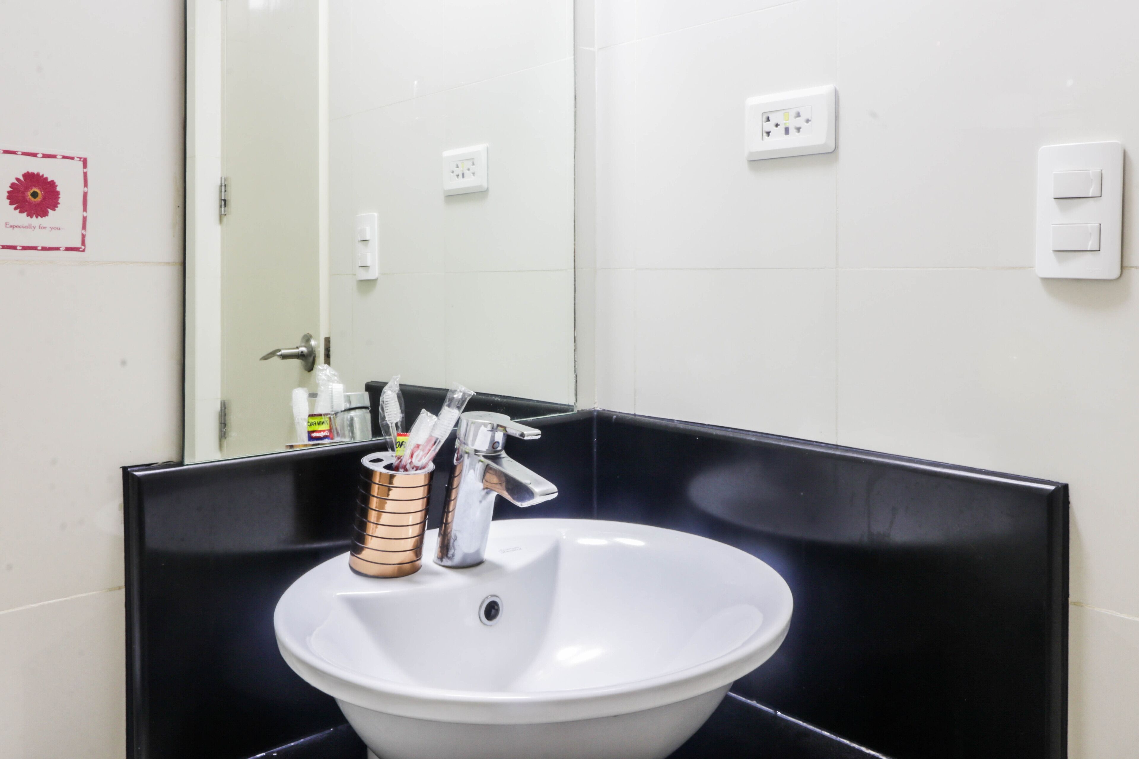 A bathroom with a white sink, black countertop, and a mirror. There are toothbrushes in a cup holder and a faucet with a modern design.