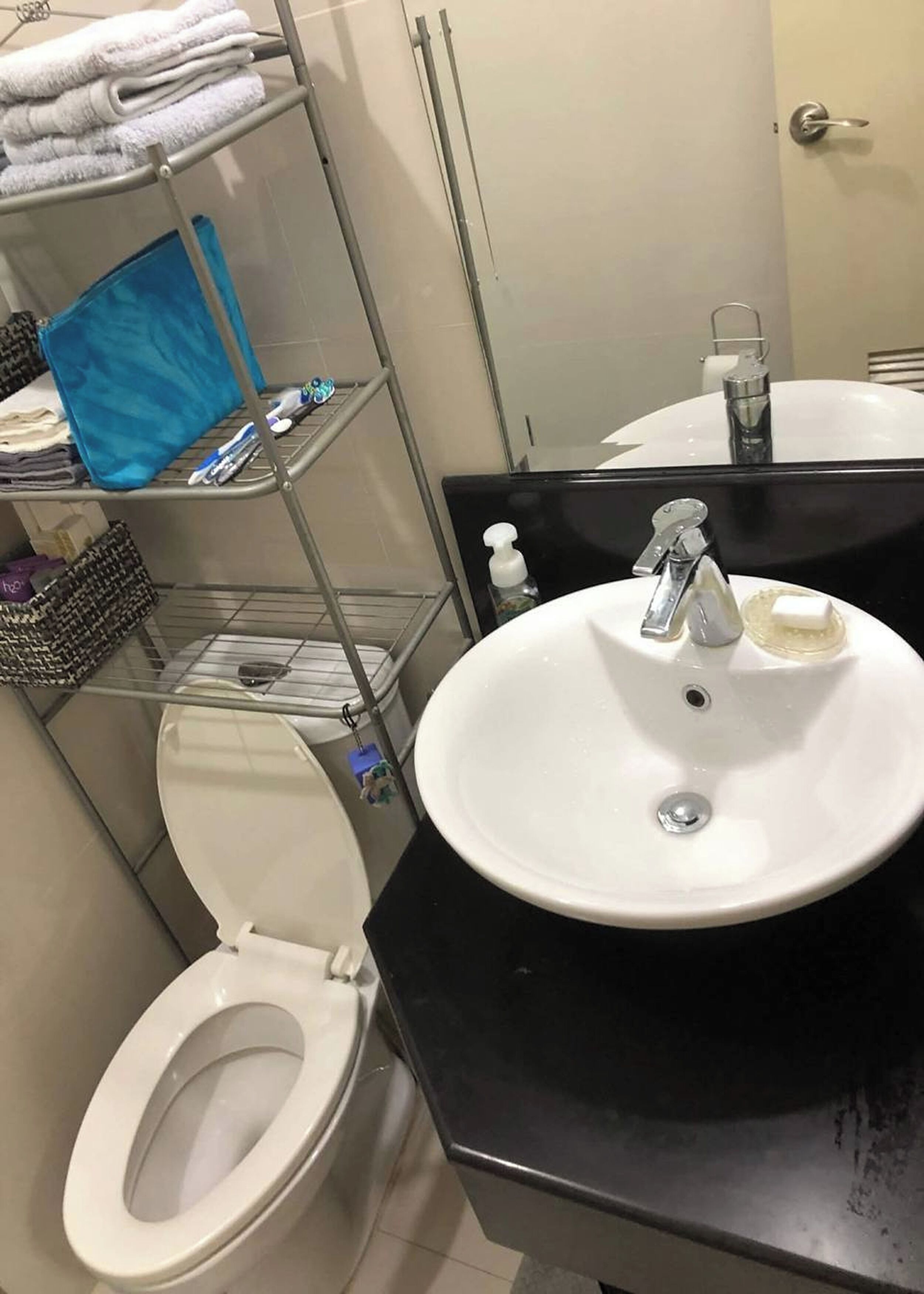 A bathroom with a white toilet, a black sink with a mirror above it, and shelves with towels and toiletries.
