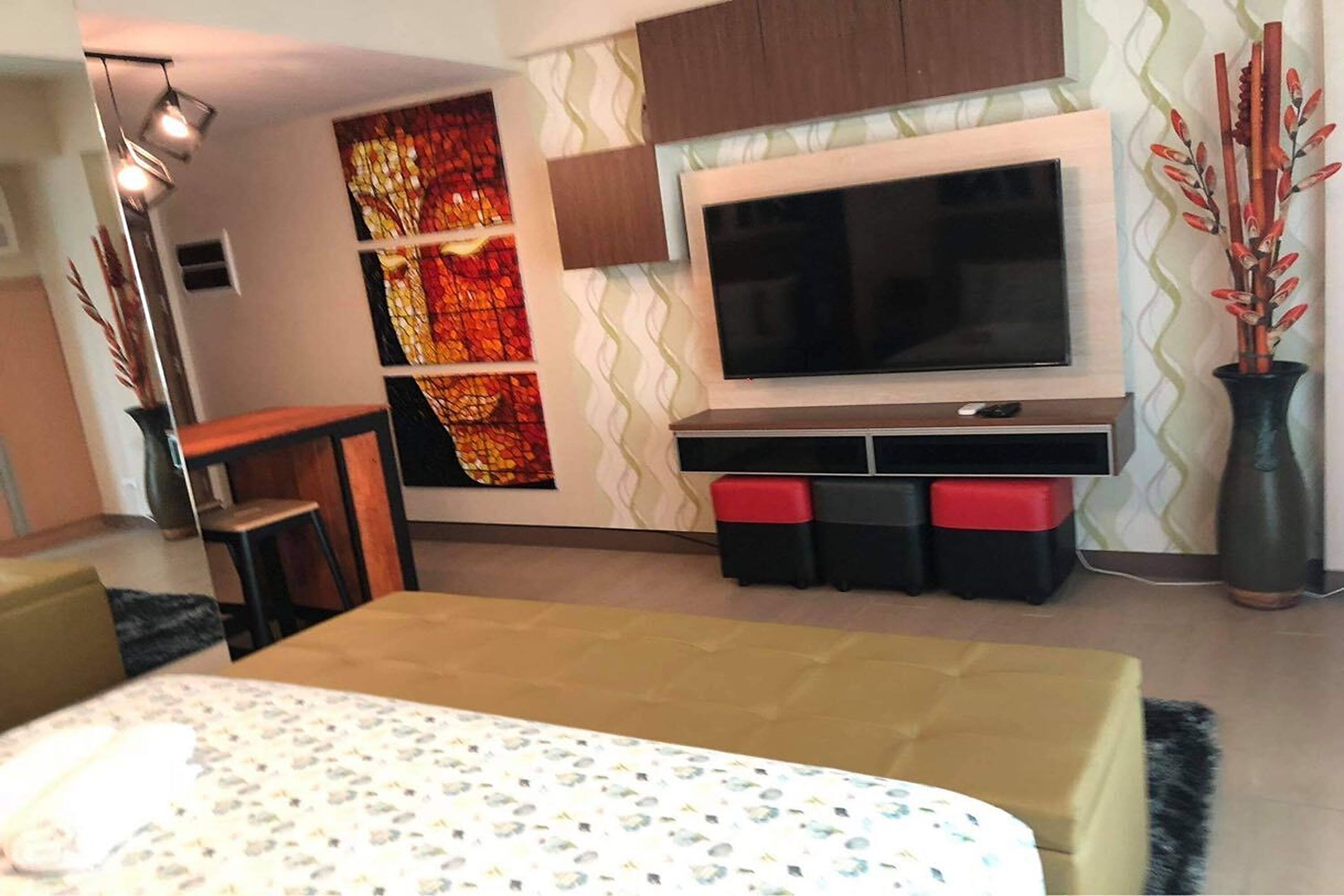 Een moderne woonkamer met een grote flatscreen-televisie, een bank, een salontafel en een decoratieve wand met een kleurrijk abstract ontwerp.