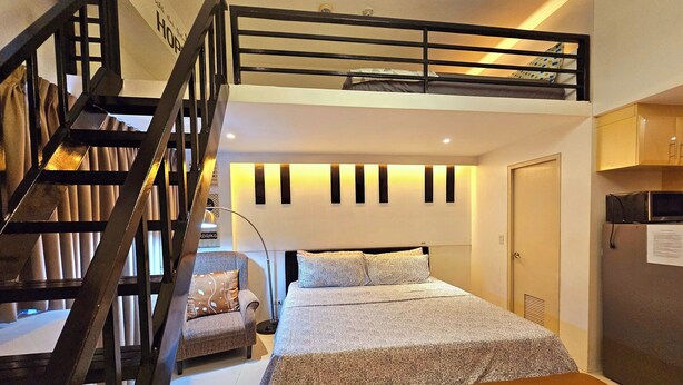 A bedroom with a bunk bed, a small chair, a desk, and a kitchenette. - PRS @ One Palm Tree Villa near T3 Airport (Pasay)