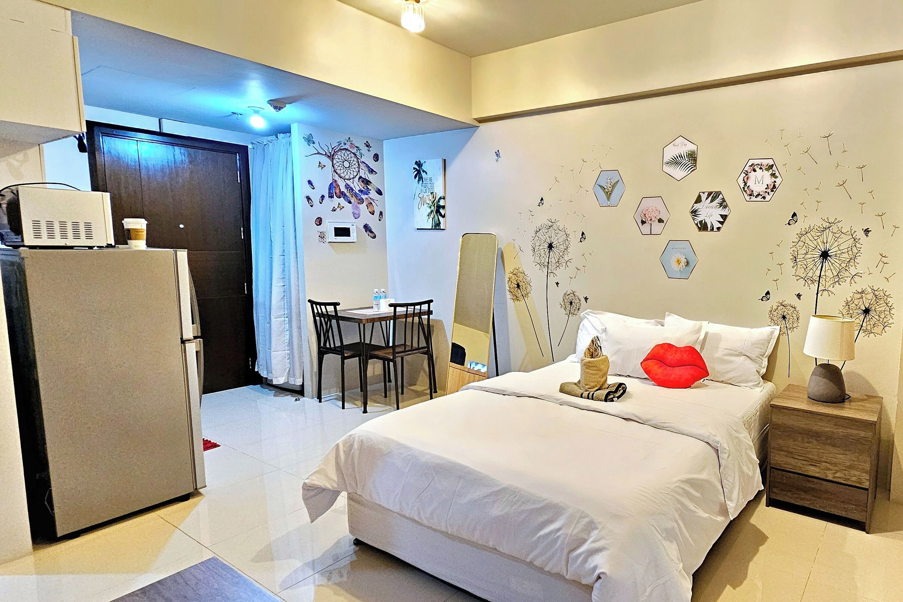 Habitación de hotel con cama, escritorio, silla, refrigerador y un muro decorado con piezas de arte hexagonales.