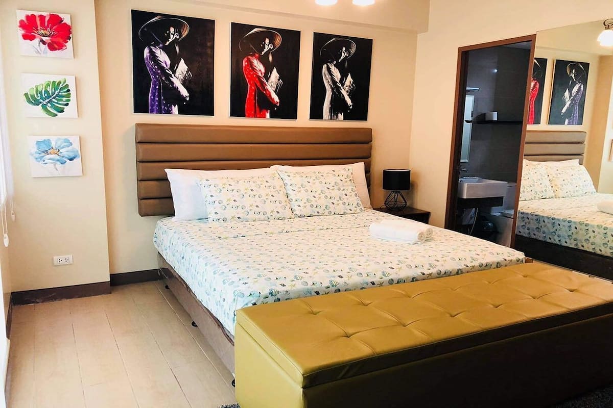 Ein Schlafzimmer mit einem großen Bett, einem Nachttisch, einem Spiegel und Bildern an den Wänden.