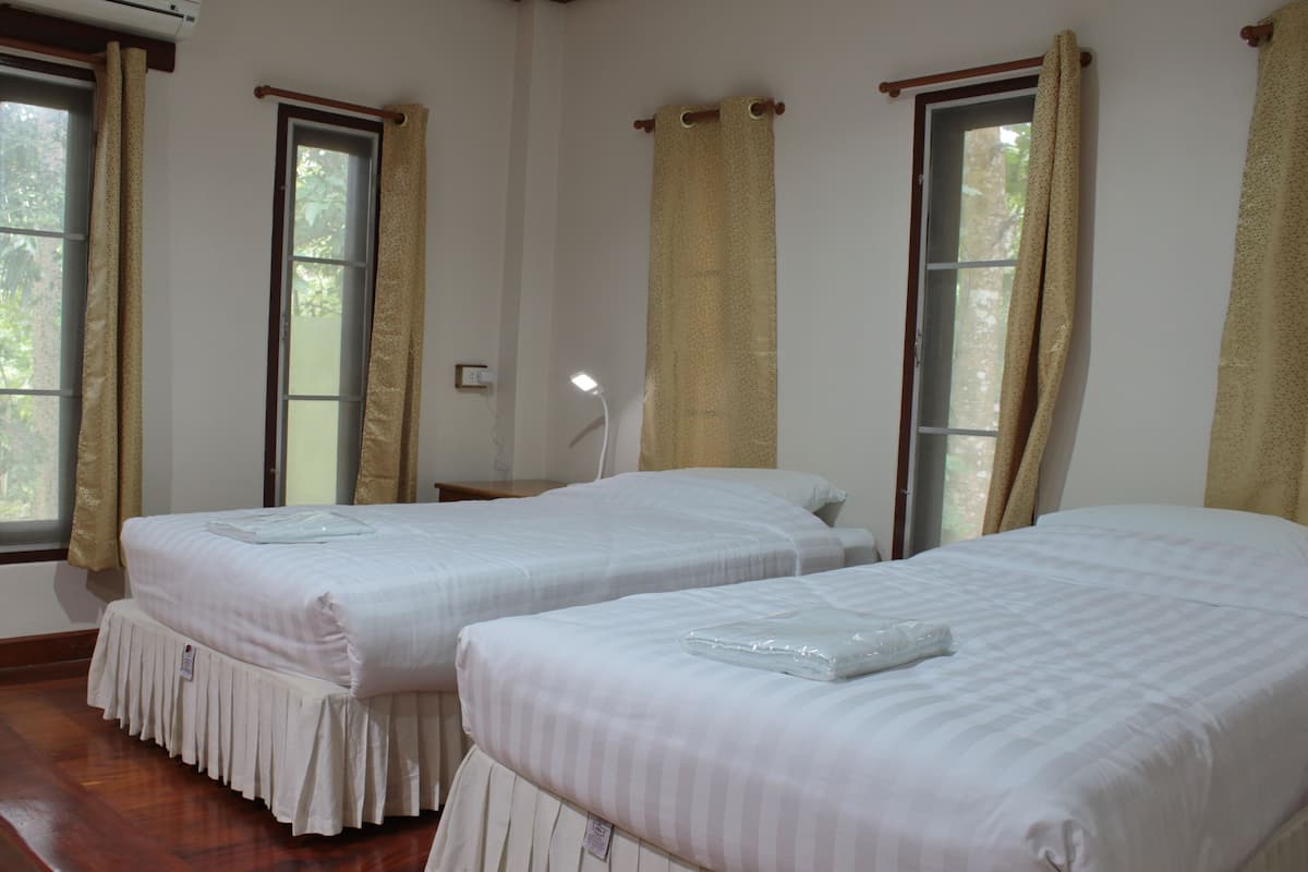 Habitación de hotel con dos camas individuales, suelo de madera y ventanas amplias con cortinas.