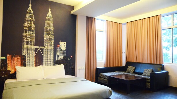 A hotel room with a large bed, a sofa, a coffee table, and a mural of the Petronas Towers. - Newland Hotel (Johor Bahru)