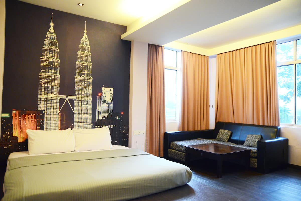 A hotel room with a large bed, a sofa, a coffee table, and a mural of the Petronas Towers.