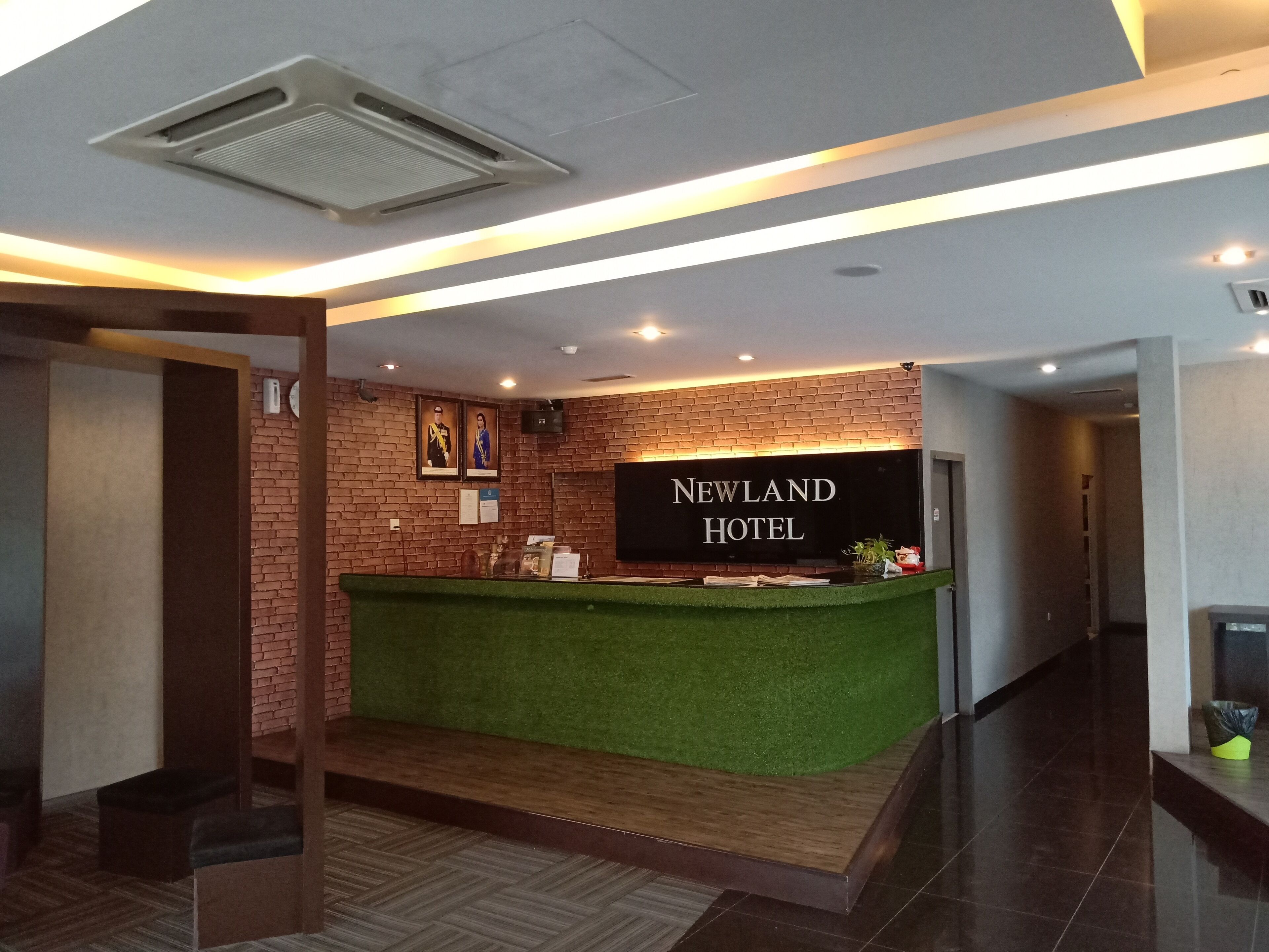 A reception desk with a green artificial grass area, a brick wall, and a sign that reads "Newland Hotel".