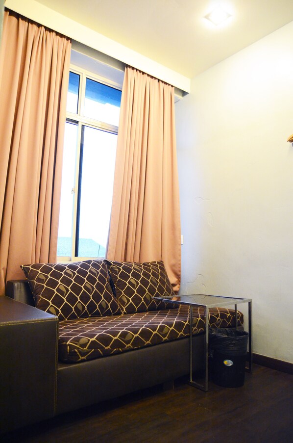A small, cozy room with a sofa, a window with curtains, and a trash bin. - Newland Hotel (Johor Bahru)