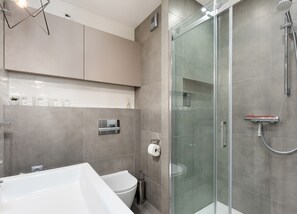 A modern bathroom with a glass shower enclosure, a white bathtub, and a toilet.
