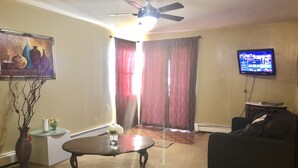 Una sala de estar con ventilador de techo, televisor, sofá, mesa de centro y un cuadro en la pared.