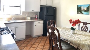 Una cocina con armarios blancos, un refrigerador negro, una estufa a gas y una mesa de comedor con sillas.