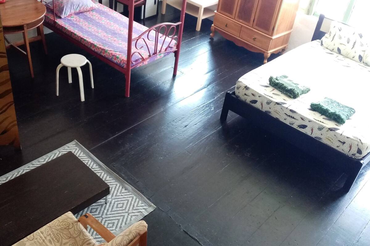 A room with a bunk bed, a small table with a stool, a patterned rug, and a wooden cabinet.