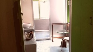 En smal hall med ett glasbord och en stol, ett vitt handfat och en grön dörr.