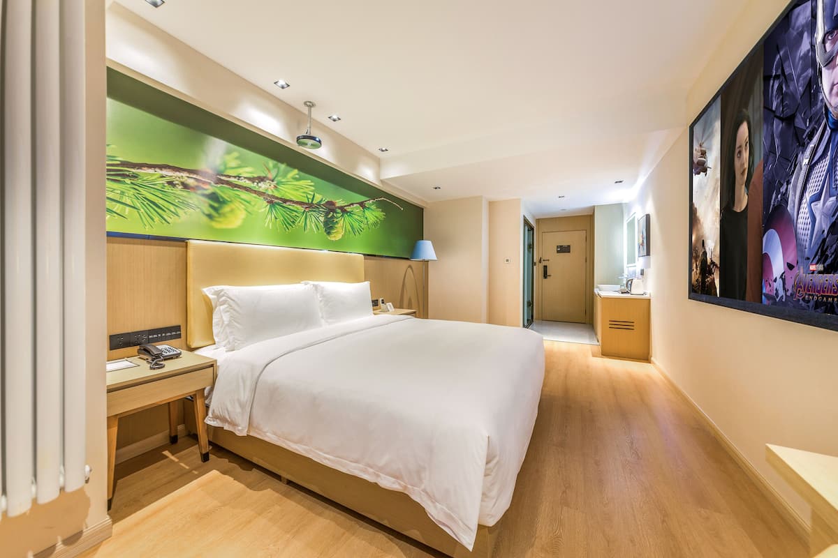 A hotel room with a large bed, a nightstand with a phone, a desk, and a painting on the wall.