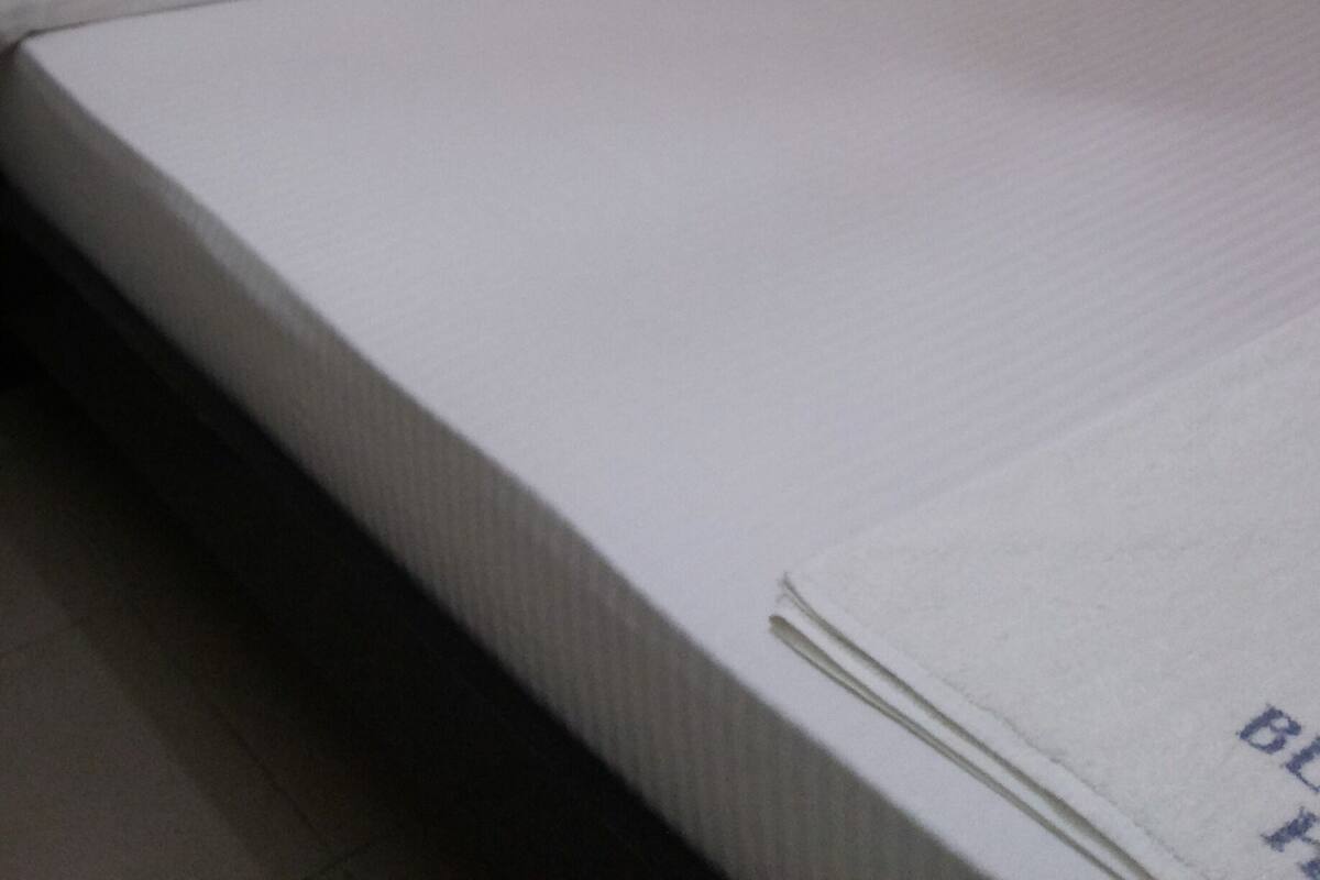 Una cama individual con colchón y almohadas blancos, cabecera negra y cortina estampada.
