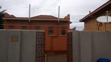 Entrada con reja a un edificio con techo rojo, una antena parabólica y un letrero que indica un baño.