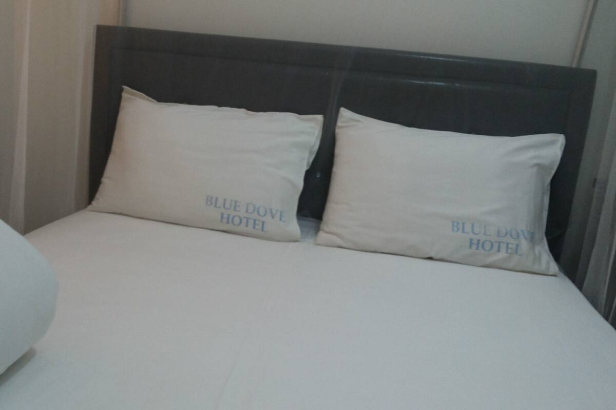 Una cama con dos almohadas, con la etiqueta 'BLUE DOVE HOTEL' y una manta blanca.