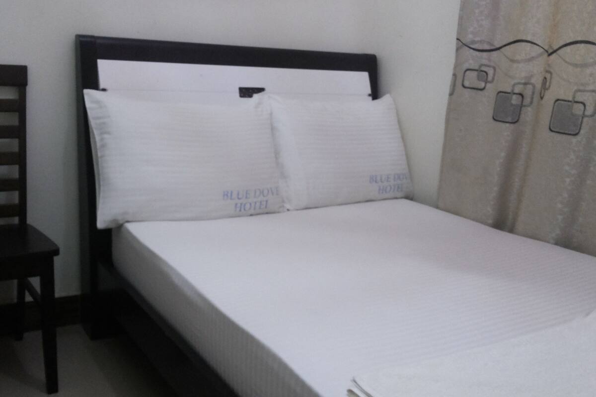 Una cama individual con ropa blanca y almohadas, un cabecero de madera y una silla.