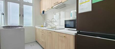 A kitchen with wooden cabinets, a microwave, a refrigerator, and a price list on the wall.