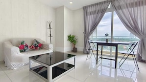 A modern living room with a white sofa, glass coffee table, and a dining table with chairs. A large window with curtains provides a view of the city. - JB City Shopping Mall Apartment (Johor Bahru)