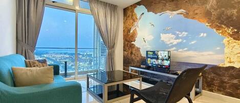 A modern living room with a large window, a sofa, a glass coffee table, a black chair, and a TV on a wall with a mural.