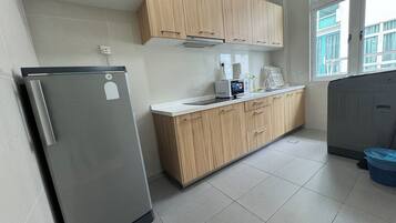 A kitchen with wooden cabinets, a stainless steel refrigerator, a microwave, and a window with a view of buildings outside.