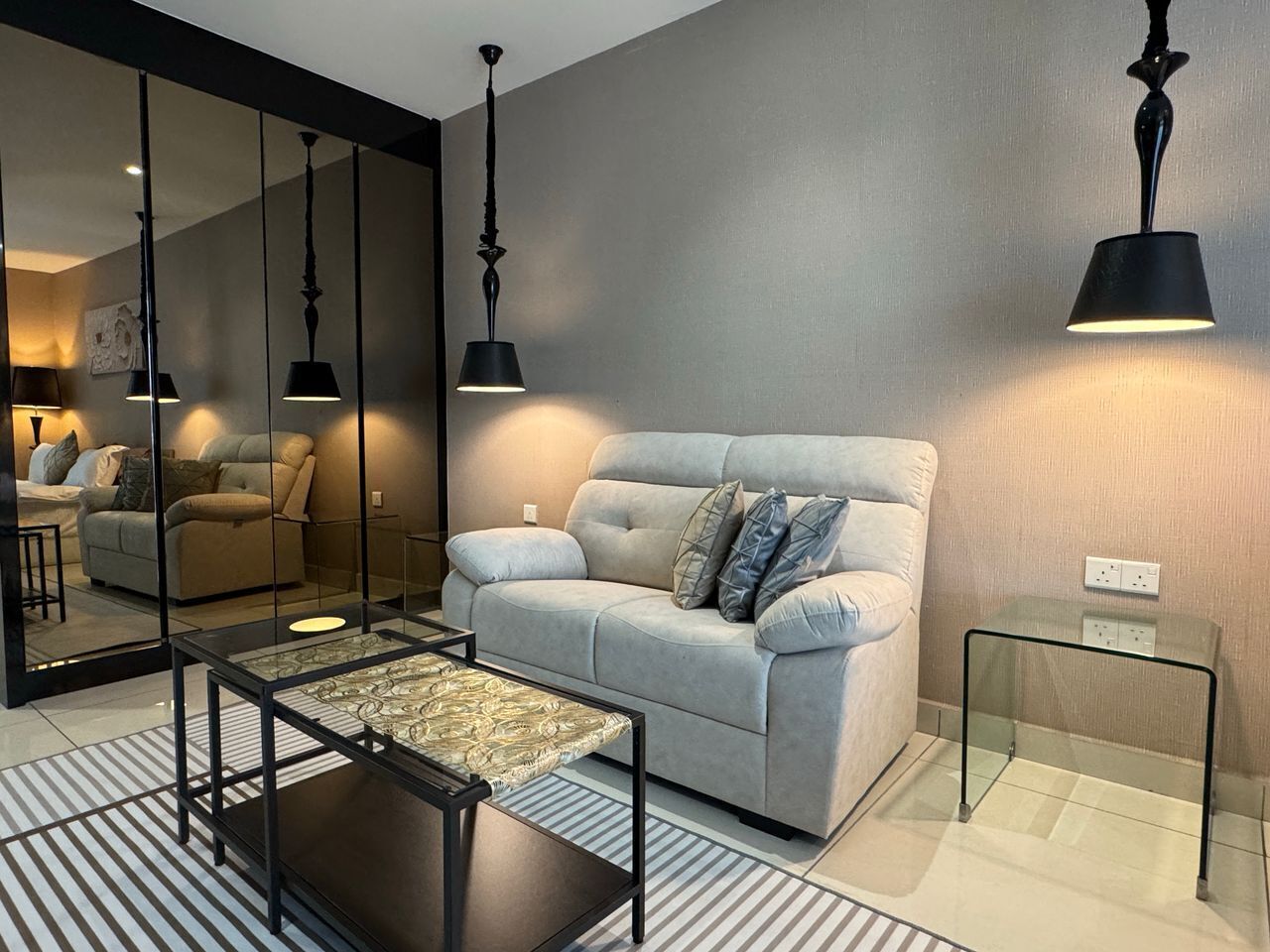 A modern living room with a sofa, a glass coffee table, and two black pendant lights.