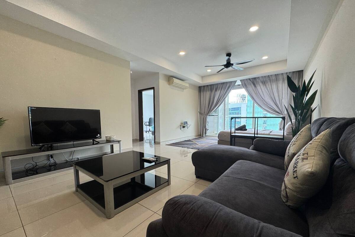 A modern living room with a flat-screen TV, a glass coffee table, and a grey sofa.