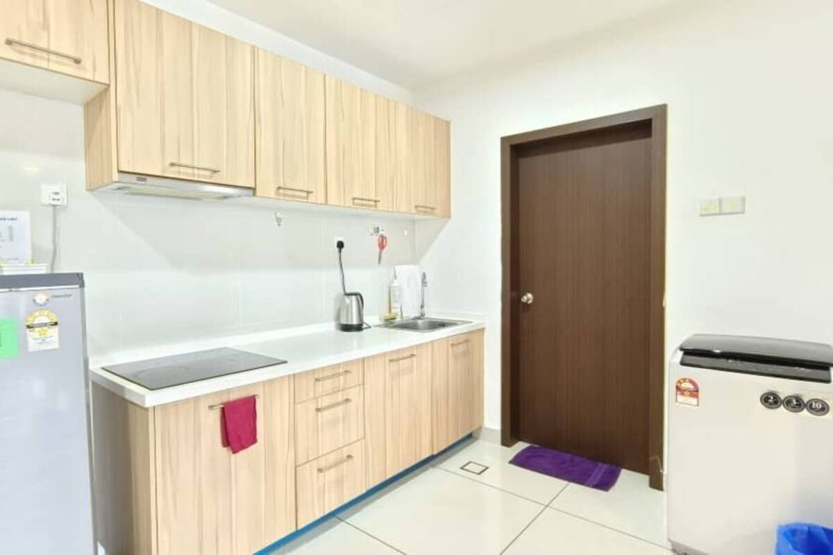 A kitchen with wooden cabinets, a stainless steel refrigerator, a sink, and a trash bin.